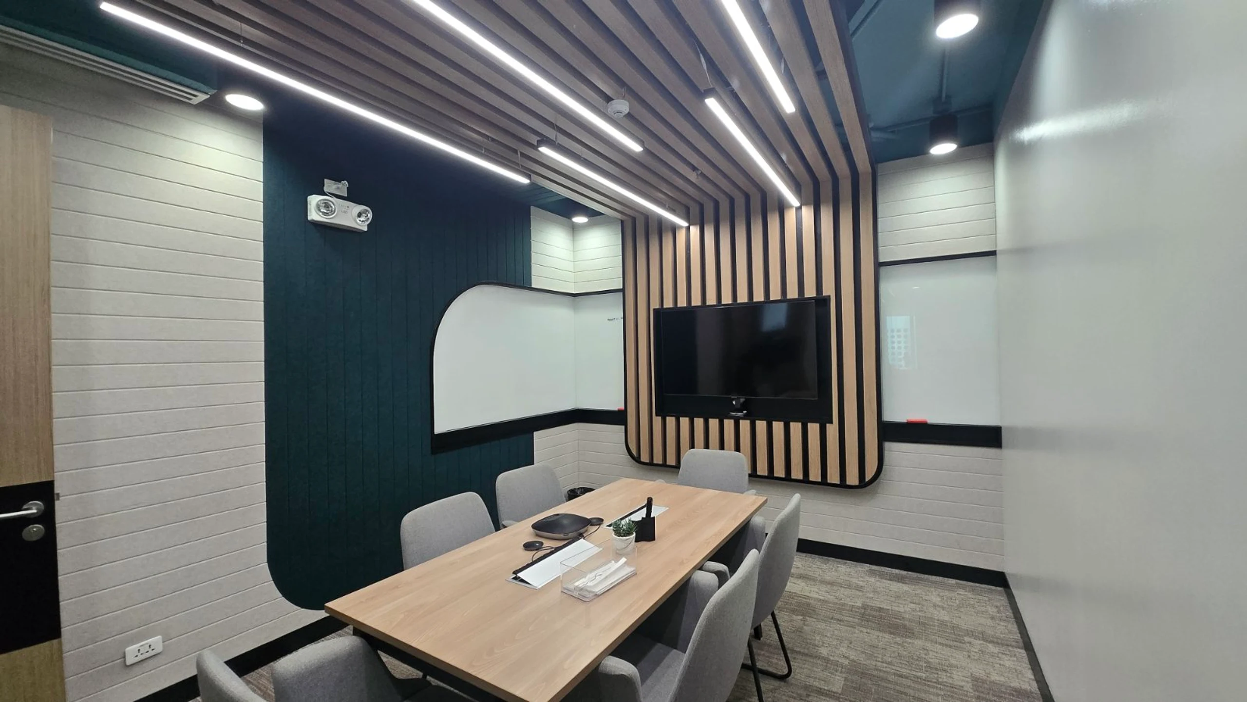 Small meeting room with a wood-slat feature wall, wall-mounted TV, and seating for six
